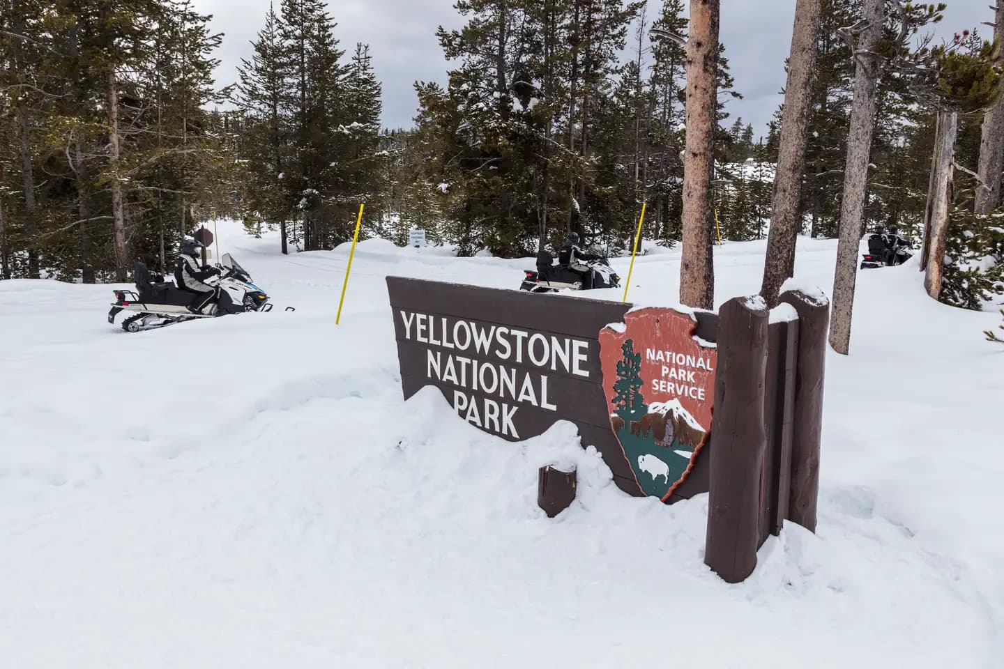 Three snowmobiles travel past an entrance sign to Yellowstone National Park