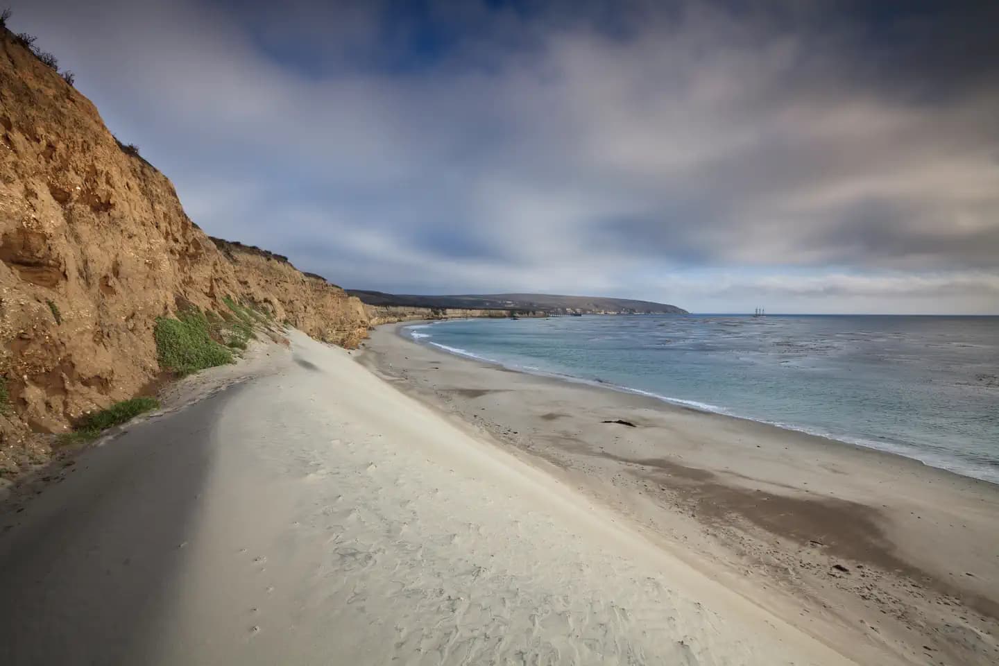 White sand dune next to a steep coastal bluff with ocean. 