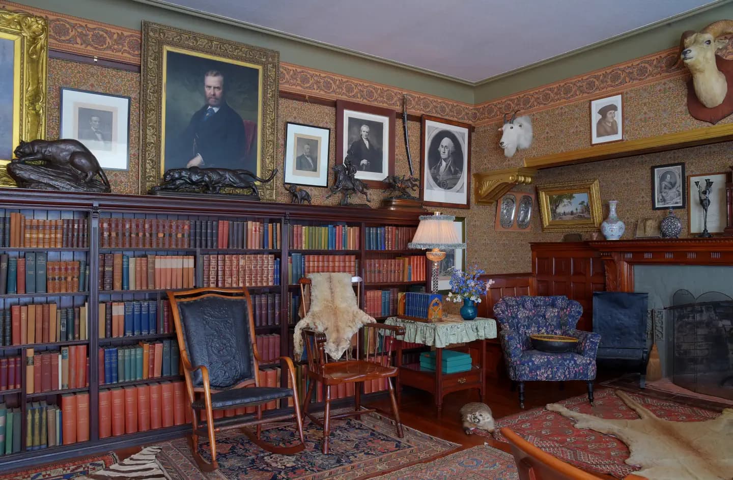 A room with books, paintings, hunting trophies, chairs, and a fireplace.