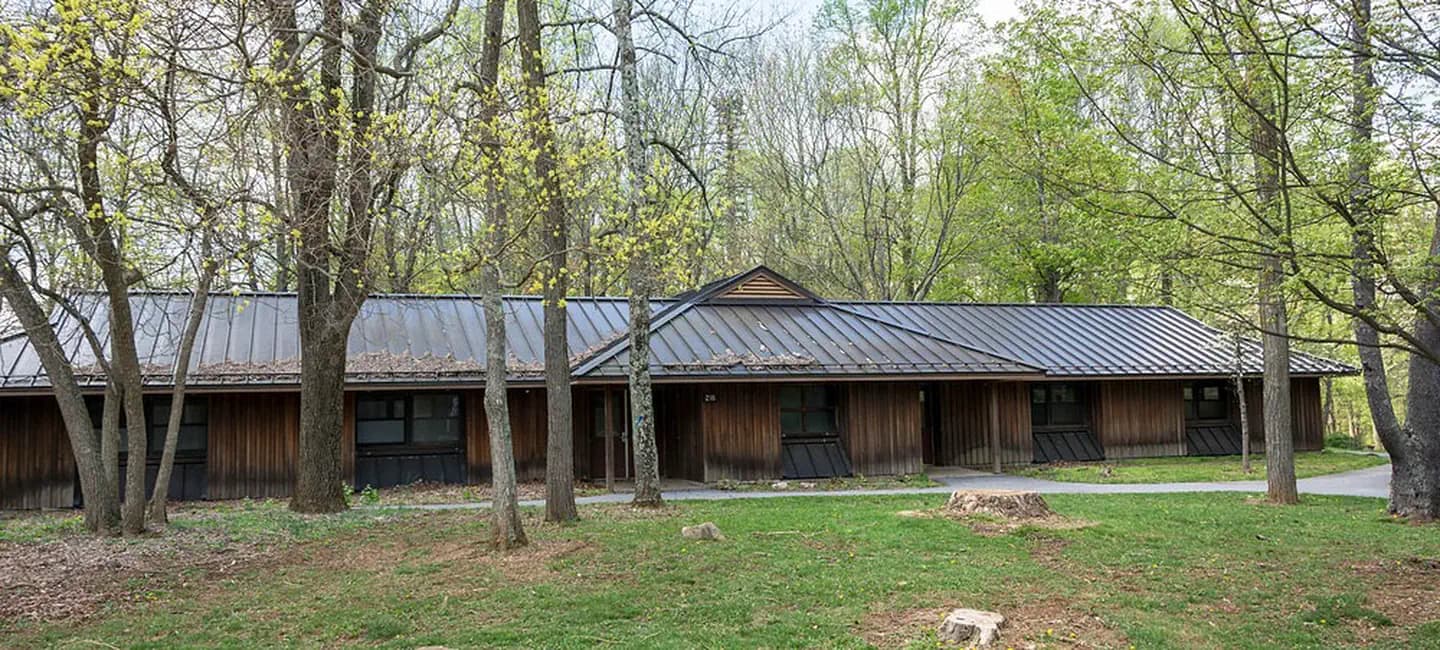Front view of one dormitory building in early spring.  Large trees are visible in front and behind the dormitory.  Each dorm accommodates 30 people and is heated.
