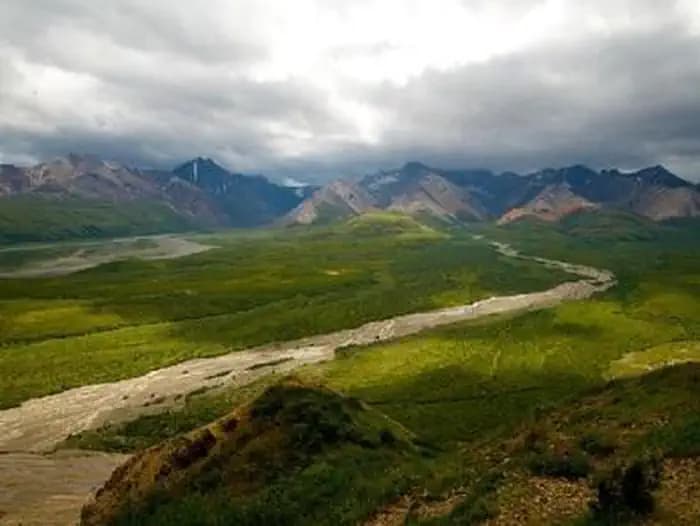 A sweeping landscape view of green hills, a braided river, and darker mountains in the distance.