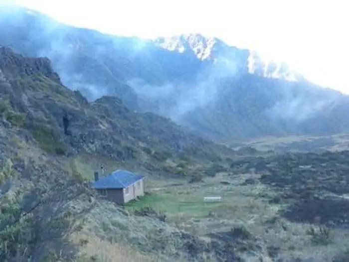view from above of cabin against a sloping cliff, fog drifting in the background