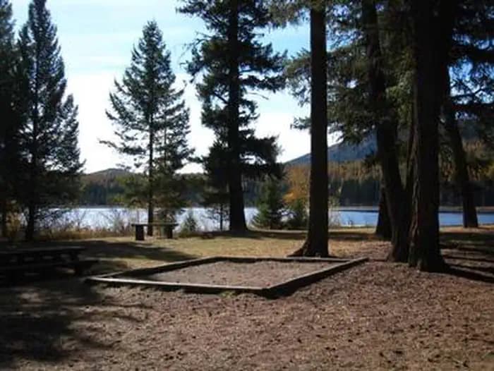 Sunlit tent pad in front of conifers in silhouette with lake and hill in background.