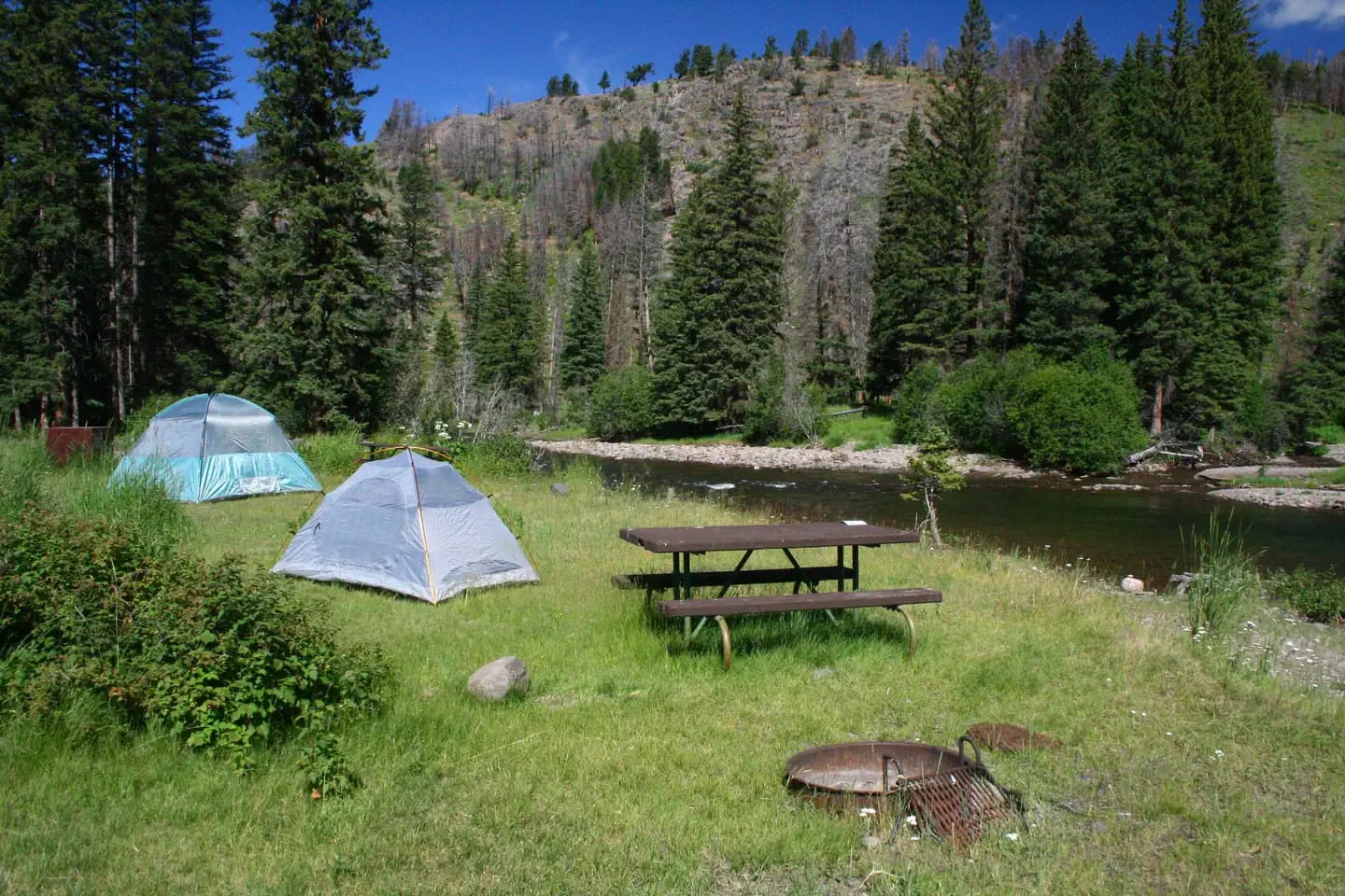 Two tents pitched at a campsite with a firepit and picnic table along Slough creek